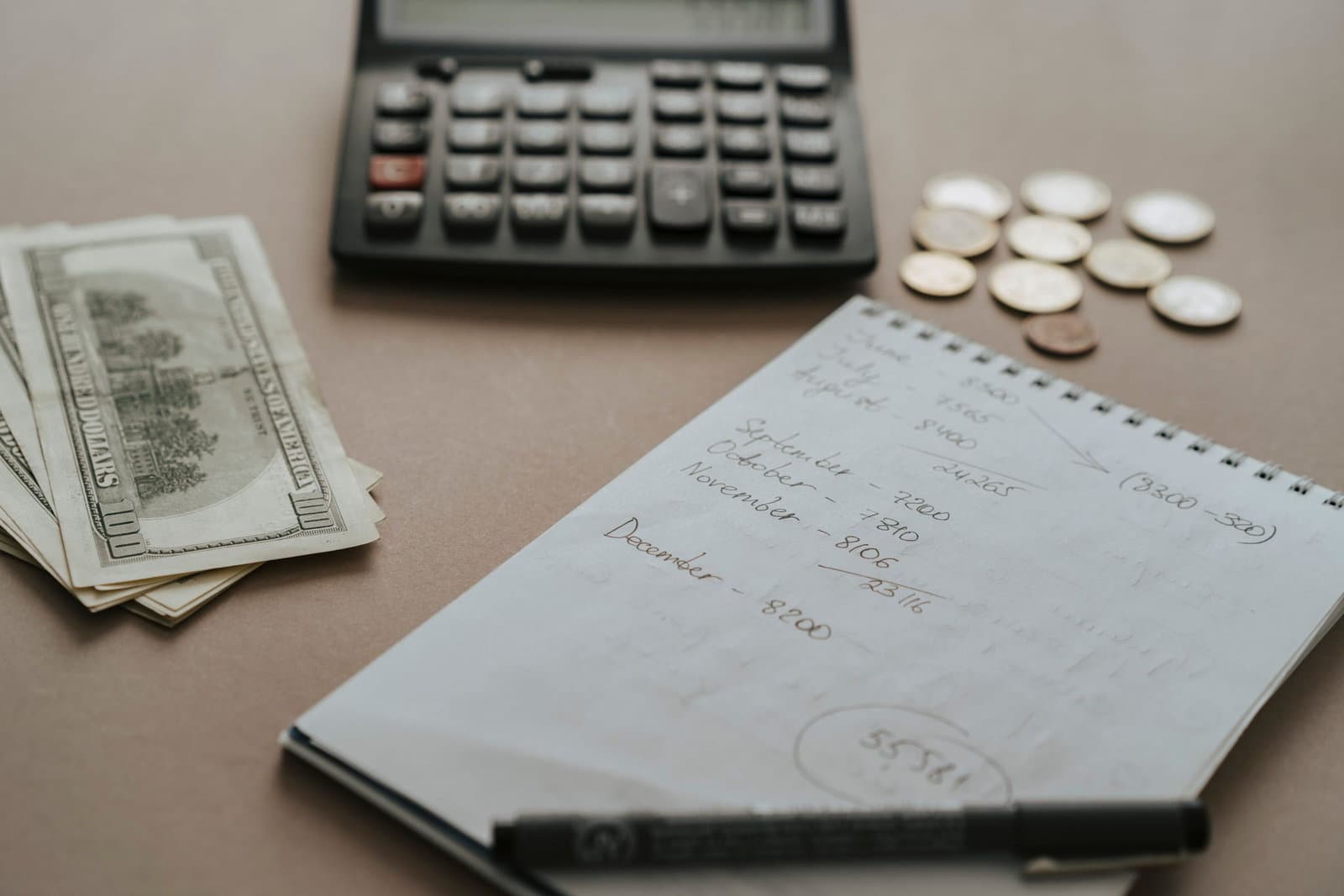 A handwritten budget page with running totals, beside a calculator, banknotes and stacked coins.