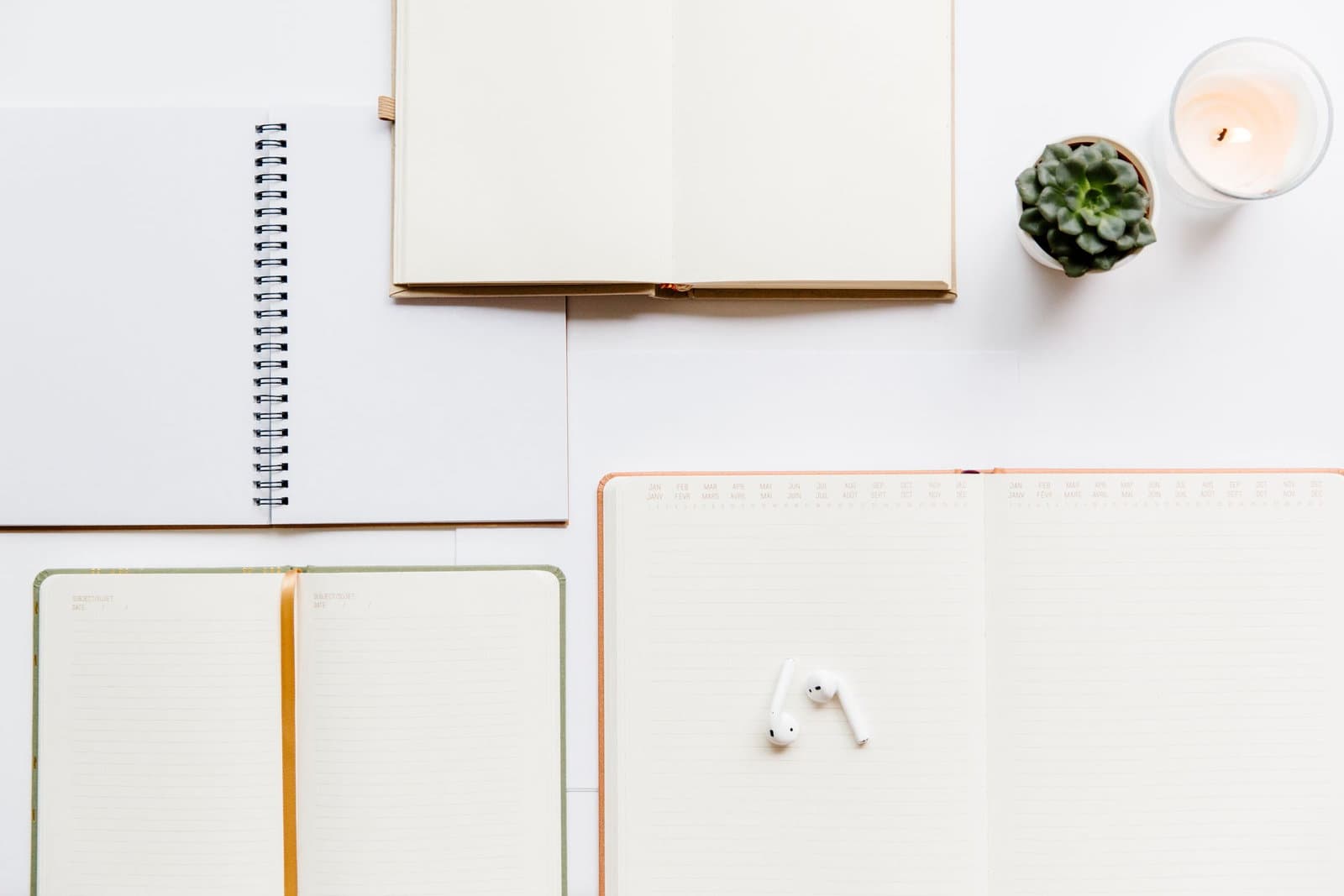 Open planner notebooks and a spiral pad laid out on a bright white desk beside a candle and a small plant.