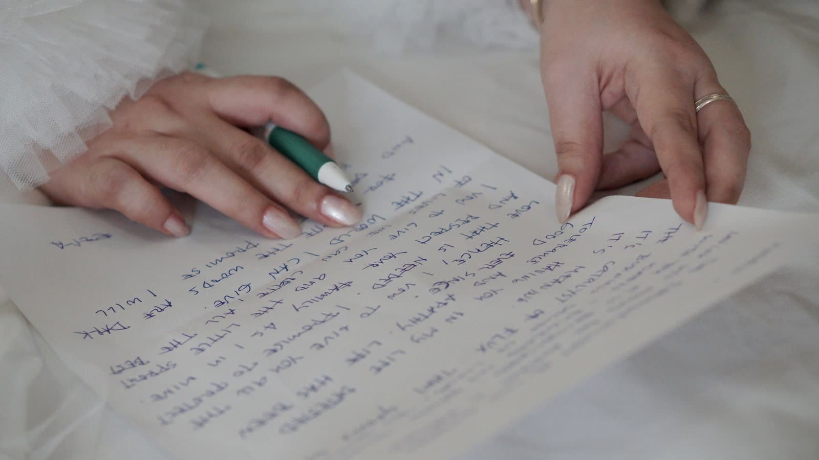 Hands hold a handwritten page and a pen over white fabric, going over the words of a ceremony reading.
