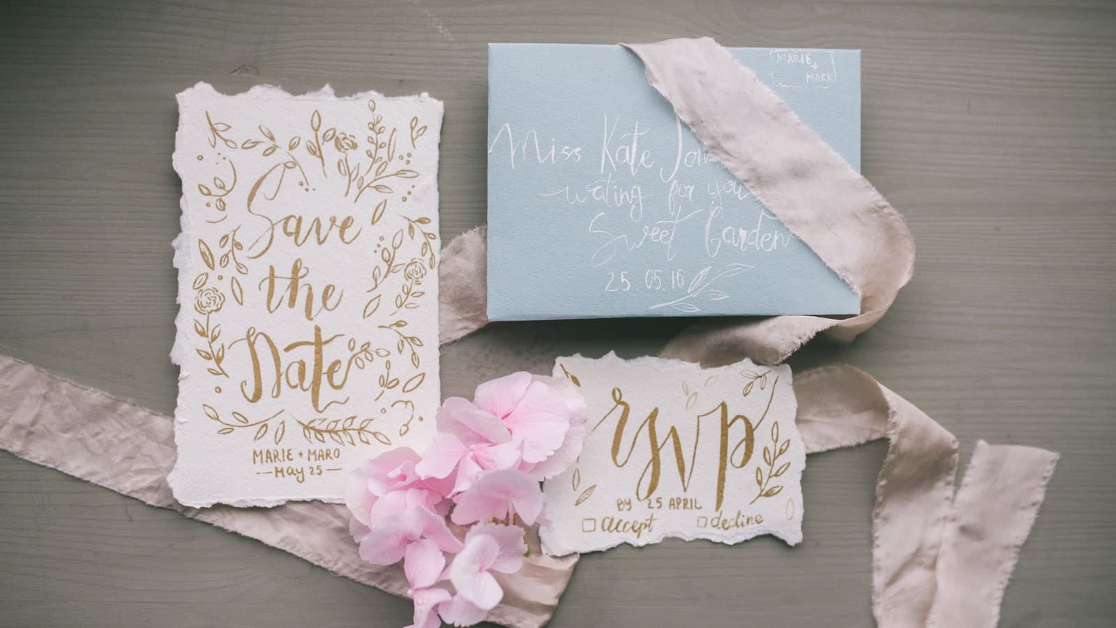 A stationery flat lay of a gold-lettered save the date card, an addressed envelope and a matching RSVP card.