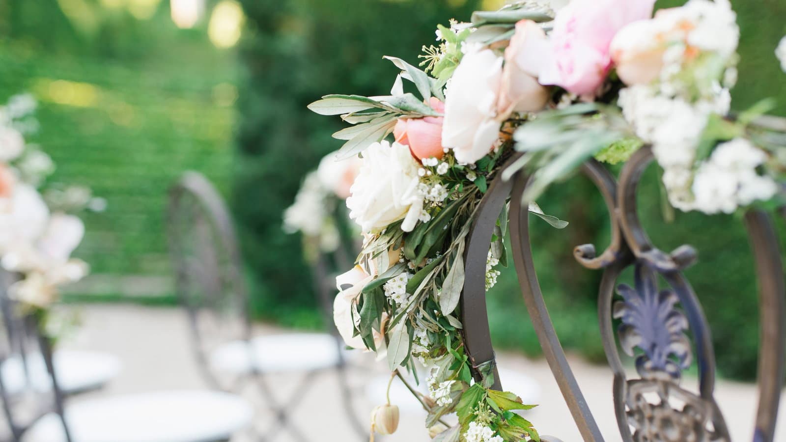 Flower-trimmed ceremony chairs set out in rows on a lawn, ready for guests to be seated.