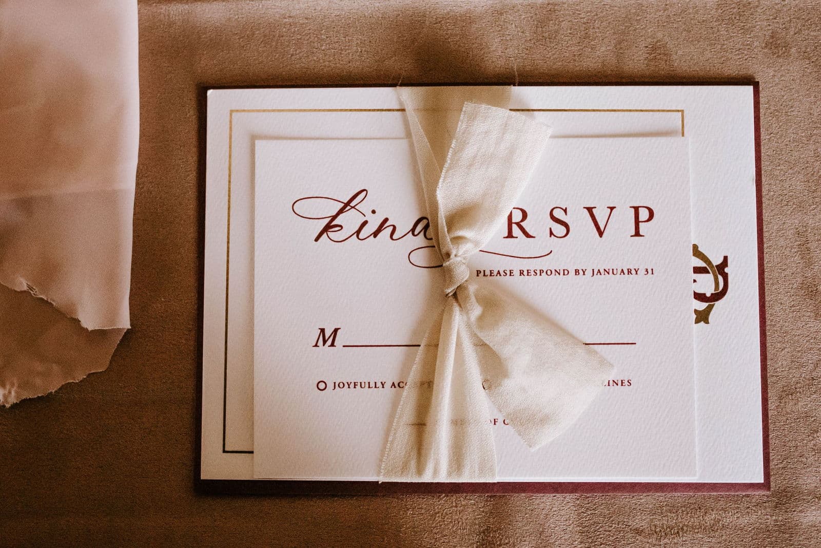 A wedding RSVP card printed with a respond-by date, tied with a soft ribbon on a warm surface.